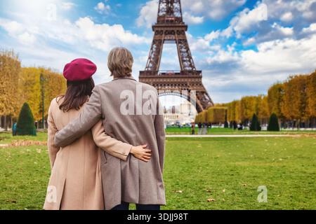 Rückansicht eines umarmten Paares, das an einem sonnigen Tag vor dem Eiffelturm in Paris, Frankreich, steht Stockfoto