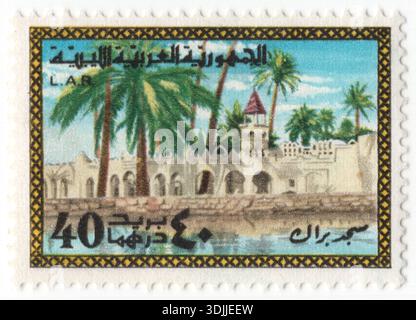 LIBYEN - 1977. Juni 1: 40 Dirham mehrfarbige Briefmarke zeigt die Sajid Brak Moschee (Masjid Brak), eine prominente religiöse Struktur in der Stadt Brak (oder Birak) in der Region Wadi al-Shatiya im Südwesten Libyens. Die traditionelle Wüstenarchitektur der Moschee umfasst ein markantes Minarett, eine weiße Kuppel und eine Reihe kleinerer Kuppeln. Diese strukturellen Elemente sind so konzipiert, dass sie eine natürliche Belüftung und Beleuchtung bieten, was im trockenen Sahara-Klima der Fezzan-Region von entscheidender Bedeutung ist Stockfoto