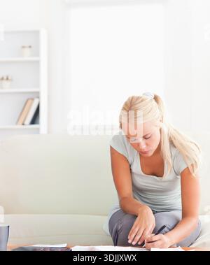 Frau in ihren 20ern, die Schreibpapiere auf dem Couchtisch zu Hause hält Stift, Kopierraum. Minimalismus, natürliches Licht, Wohnzimmer, hell, Focus, Dokument Stockfoto