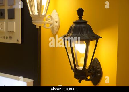 An der gelben Wand hängen dekorative Wandlaternen mit brennenden Glühbirnen Stockfoto