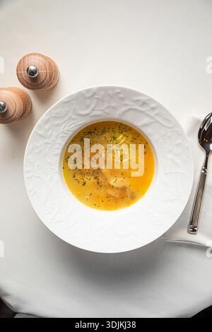 Klare Hühnersuppe mit Kräutern in einer weißen Schüssel Stockfoto