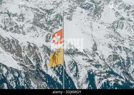 Fahnen der schweiz und graubünden flattern vor einer schneebedeckten Berglandschaft in davos Stockfoto