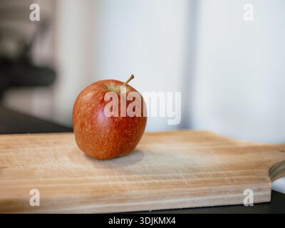 Bild eines roten Apfels auf einem Holzbrett, mit verschwommenem Hintergrund drinnen. Nützlich für gesunde Ernährung, Obst und Ernährung Kampagnen, Rezepte, Landwirtschaft Stockfoto