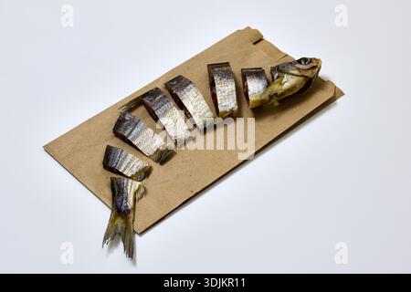 Nahaufnahme Räucherfisch, in Stücke geschnitten, liegt auf einem braunen Papierbeutel. Die Szene fängt einen Fisch-Snack ein, perfekt als Vorspeise mit Bier, eine köstliche Suppe Stockfoto