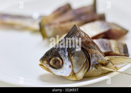 Dieses Bild zeigt eine Nahaufnahme eines getrockneten Fischkopfes, der auf einem weißen Teller serviert wird und einen detaillierten Blick auf dieses traditionelle asiatische Meeresfrüchte-del bietet Stockfoto
