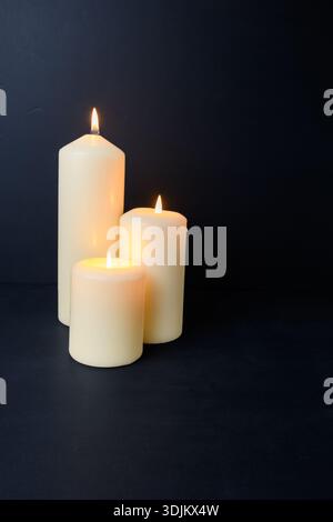 Drei beleuchtete Kerzen mit warmem Licht auf dunklem Hintergrund, gemütliches Spa-Ambiente und Kopierraum. Stockfoto