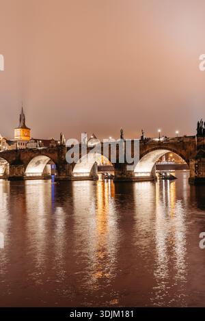 Karlsbrücke bei Nacht im Winter vom Flussufer der Kleinstadt aus gesehen. Moldau Fluss, Touristen wandern Stockfoto