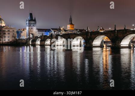 Karlsbrücke bei Nacht im Winter vom Flussufer der Kleinstadt aus gesehen. Moldau Fluss, Touristen wandern Stockfoto