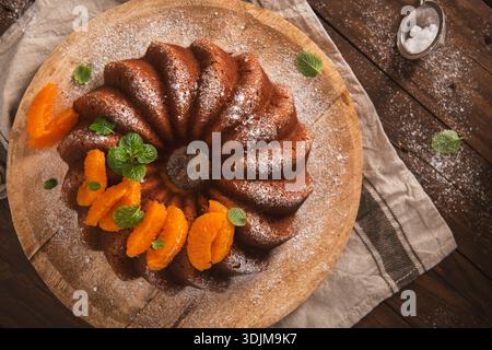 Ein frisch gebackener Zitrus-Biskuitkuchen liegt auf einer rustikalen Holzplatte mit einer tiefen goldenen Kruste und einer weichen Textur. Warmes natürliches Licht, Highlights t Stockfoto