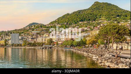 Blick auf die Uferpromenade von Montreux am Genfer See, Schweiz, mit der Stadt, dem Ufersteg und bewaldeten Hügeln im Hintergrund Stockfoto
