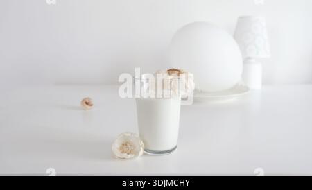 Minimales weißes Stillleben mit einem Glas Milch und Knoblauch auf dem Tisch, trübe weiße Zusammensetzung Stockfoto