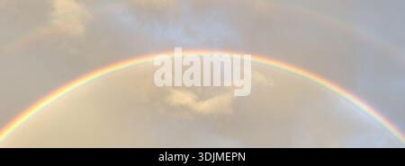 Regenbogen erscheint am Himmel nach Regen und füllt die Szene mit Farbe gegen Wolken am Nachmittag. Stockfoto