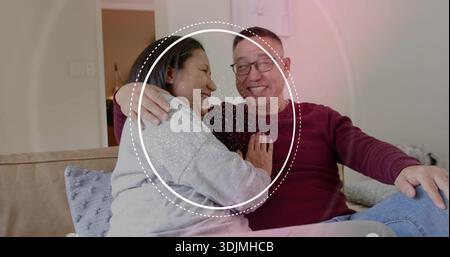 Sitzendes älteres Paar, das sich zu Hause auf einem beigefarbenen Sofa stützt, trägt einen kastanienbraunen Pullover mit gepunktetem Überzug Stockfoto