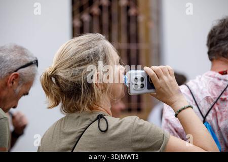 BANGKOK, THAILAND-21. JAN 2026: Seniorin mit gebundenem blondem Haar Trinkwasser aus einer Plastikflasche und Erkundung des thailändischen Tempelseitenprofils Stockfoto