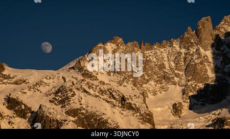 Eine Teleaufnahme des Mondes über dem schneebedeckten Mont-Blanc-Massiv bei Sonnenuntergang, fotografiert von der anderen Seite des Chamonix-Tals in Haute-Savoie, Frankreich. Stockfoto