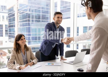 Zwei positive Geschäftsleute schütteln die Hände über den Konferenztisch Stockfoto