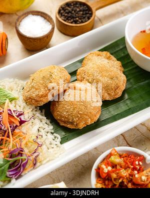 Bei einer Nahaufnahme werden drei goldbraune, knusprige gebratene Patties auf einem Bananenblatt gezeigt. Begleitet von flauschigem weißem Reis, einer lebhaften Salatmischung und Stockfoto