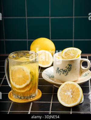 Eine Nahaufnahme zeigt zwei Portionen Limonade, eine in einem hohen Glas mit Eis- und Zitronenscheiben, die andere in einer Vintage-Tasse. Frische Zitronen, einschließlich Stockfoto