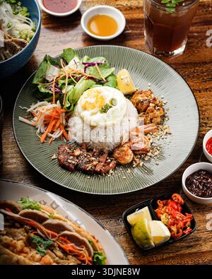 Ein köstlicher vietnamesischer com Tam oder gebrochener Reisteller mit Spiegelei, gegrilltem Schweinefleisch, herzhaften Garnelen, frischem Salat und eingelegtem Gemüse. Serviert Stockfoto