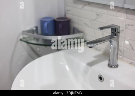 Modernes Badezimmer mit sauberem, weißem Keramikwaschbecken und glänzendem Chromarmatur. Einfaches Design für tägliche Hygiene mit minimalistischem Glasboden und Stockfoto