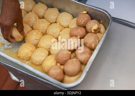 Nahaufnahme der Bäckerhand sorgfältig anordnen der Brotkugel für den Rohkäse zum Backen in Metallblech. Der zufriedenstellende Prozess unterstreicht die handwerkliche Zubereitung der Speisen Stockfoto