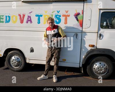 Ein junger Mann posiert vor einem weißen Food Truck, Avia A21 Food Truck, mit bunten tschechischen Text „Ledová Tříšť“ (Eis schlampig) Stockfoto