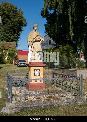 Eine Steinstatue des heiligen Johannes von Nepomuk mit einem Halo von fünf Sternen, auf einem Sockel in einem Metallzaun Stockfoto