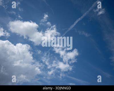 Weiße Cumuluswolken und mehrere Flugzeugdampfpfpfpfade (Kondensstreifen) an einem klaren blauen Himmel an einem hellen Tag Stockfoto