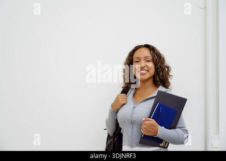 Porträt einer lächelnden, selbstbewussten jungen Frau mit Laptop und Buch, die in der Nähe der Universität steht Stockfoto