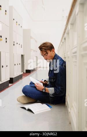 Junge Studentin, die studiert, während sie auf dem Boden im Universitätskorridor sitzt Stockfoto