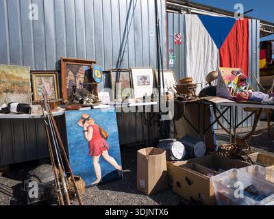 Verschiedene Antiquitäten, Gemälde und Sammlerstücke werden auf Tischen auf einem Flohmarkt im Freien vor einer Metallwand und einer Flagge der Tschechischen Republik ausgestellt. Stockfoto