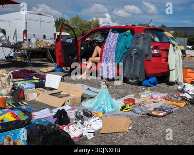 Ein rotes Auto, das als Ausstellung für den Verkauf von Kleidung auf einem Flohmarkt im Freien verwendet wird, mit verschiedenen Spielzeugen, Schuhen und Haushaltsgegenständen auf dem Boden verteilt Stockfoto