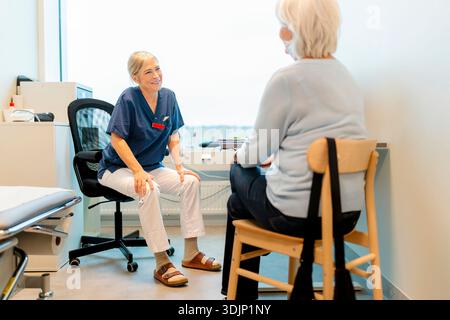 Lächelnde leitende Ärztin im Gespräch mit dem Patienten während sie im Krankenhausbüro sitzt Stockfoto