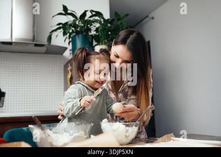 Eine Mutter und ihre Tochter arbeiten in der Küche, um etwas Besonderes zu backen. Sie mischen Zutaten und teilen fröhliche Momente, während sie gemeinsam Speisen zubereiten. Stockfoto