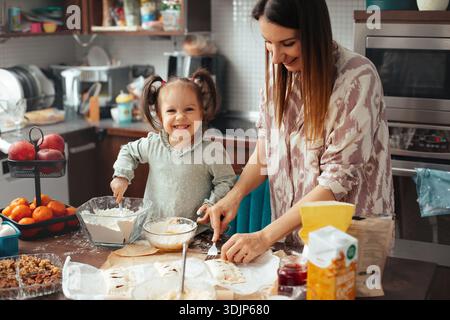 Zwei Leute arbeiten zusammen in einer Küche und machen Essen. Der Erwachsene hilft dem Kind, Zutaten zu mischen und Teig zu Formen. Sie lächeln und genießen sich gegenseitig Stockfoto