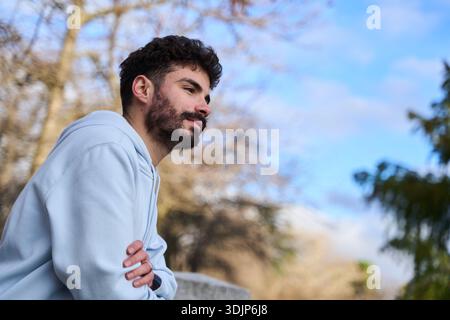 Bärtiger Mann, der frische Luft in einem Stadtpark genießt und nachdenklich wegblickt. Lifestyle-Porträt mit Reflexion und ruhiger Freizeit Stockfoto