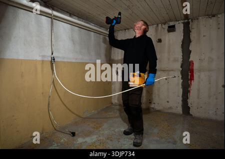 Elektriker bohrt die Decke beim Verlegen von Elektrokabeln während der Renovierung des Innenraums mit Elektrowerkzeugen und Schutzhandschuhen Stockfoto