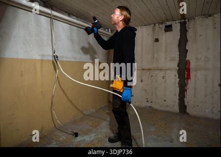 Elektriker bohren in der Decke für die Elektrokabelinstallation während der Innenraumsanierung mit Bohrmaschine und Schutzhandschuhen Stockfoto