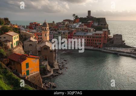 Blick auf farbenfrohe Gebäude stürzt hinunter zum Hafen, wo das türkisfarbene Wasser auf den mittelalterlichen Turm in Vernazza, Ligurien, Italien trifft. Stockfoto