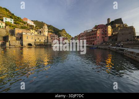 Blick auf farbenfrohe Gebäude, die den Hügel hinunter in den Hafen stürzen, reflektieren goldenes Licht auf dem ruhigen Wasser, Vernazza, Ligurien, Italien. Stockfoto