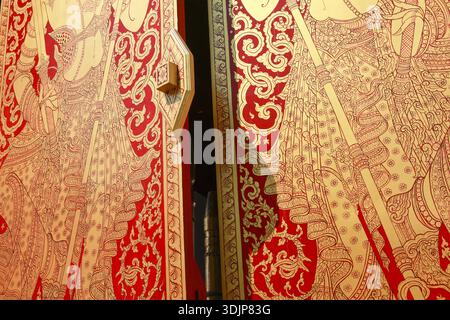 Verzierte, traditionelle asiatische Holztür mit einem komplizierten Rot- und Goldgemälde. Dieses kulturelle Kunstwerk zeigt eine mythische Figur, ein klassisches Beispiel für Thai Stockfoto