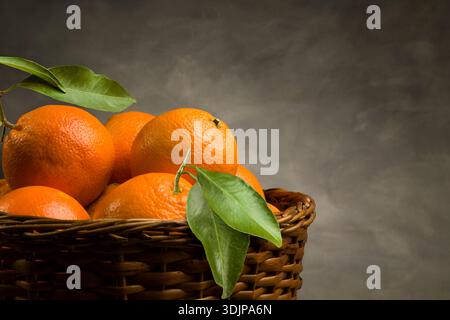 Ein Haufen reifer, frischer Orangenfrüchte in einem Korb auf dunklem Hintergrund. Stockfoto