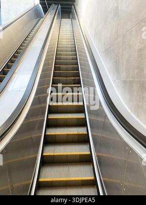 Die moderne Rolltreppe erhebt sich in einem stilvollen Gebäude mit metallischen Oberflächen und beleuchteten Stufen, die urbanes Design und architektonische Eleganz hervorheben Stockfoto