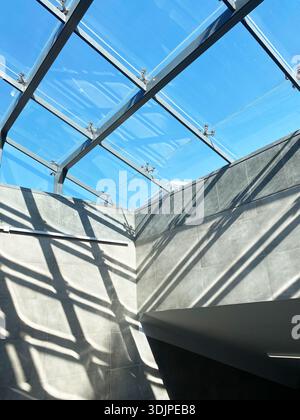Hell-Dunkel-Effekt durch Sonnenlicht, das durch die Glasdecke filtert, erzeugt markante geometrische Schatten auf grauen Wänden, die moderne Architektur hervorheben Stockfoto