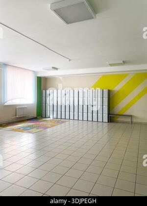 Der Flur der Grundschule zeigt Ablagefächer vor einer hellen Wand, mit farbenfrohem Boden und natürlichem Licht, die eine einladende Atmosphäre schaffen Stockfoto