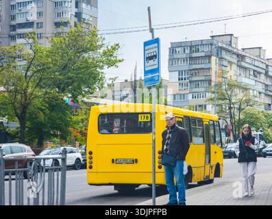 Kiew, Ukraine - 6. Mai 2023 : die Leute warten und laufen an einer Bushaltestelle, während ein gelber Marschutka auf einer belebten Kiewer Straße vorbeifährt und jeden Tag urba festnimmt Stockfoto