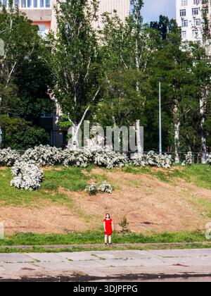 Kiew, Ukraine - 6. Mai 2023 : Frau, die an einem Betonkanal steht, vor einem Hintergrund von grünen Bäumen, blühenden Büschen und Stadtgebäuden, Ref Stockfoto