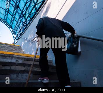 Kiew, Ukraine - 6. Mai 2023 : ältere Frau mit Gehstock und Einkaufstaschen klettert in Kiew Betontreppen und zeigt Ausdauer und städtische Unruhe Stockfoto