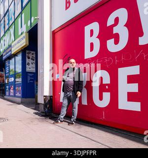 Kiew, Ukraine - 6. Mai 2023 : Mann steht an der roten Graffiti-Wand neben einem Geschäftsgebäude auf einem Kiewer Bürgersteig, ungezwungene urbane Alltagsszene Stockfoto