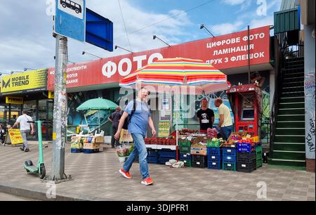 Kiew, Ukraine - 6. Mai 2023 : ein Mann, der an einem farbenfrohen Kiewer Obst- und Gemüsestand an einer Bushaltestelle und Schaufensterfronten vorbeiläuft und den alltäglichen städtischen mar erfasst Stockfoto